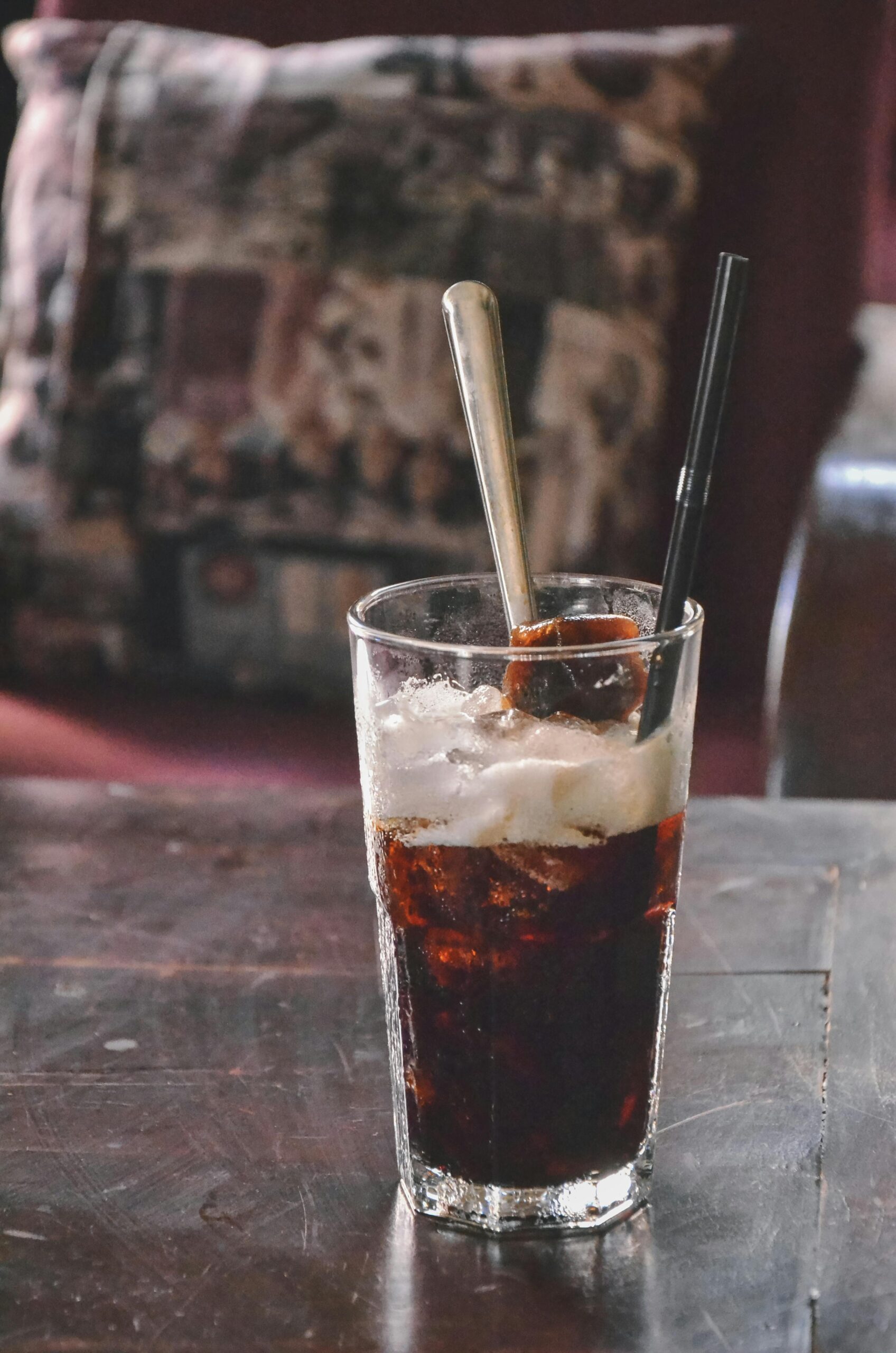Close-up of a refreshing iced drink with cream, in a glass with a straw, indoor setting.